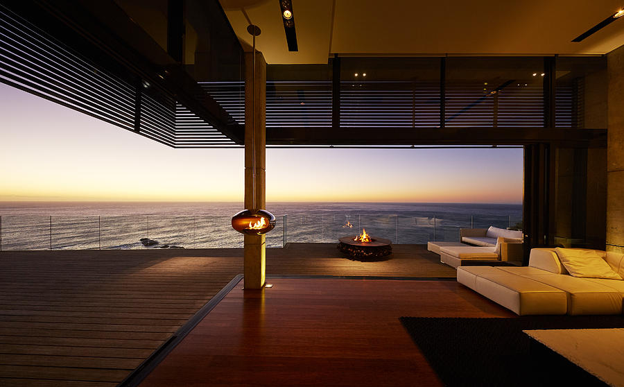 Fire pit and hanging fireplace on modern luxury patio with sunset ocean view Photograph by Caia Image