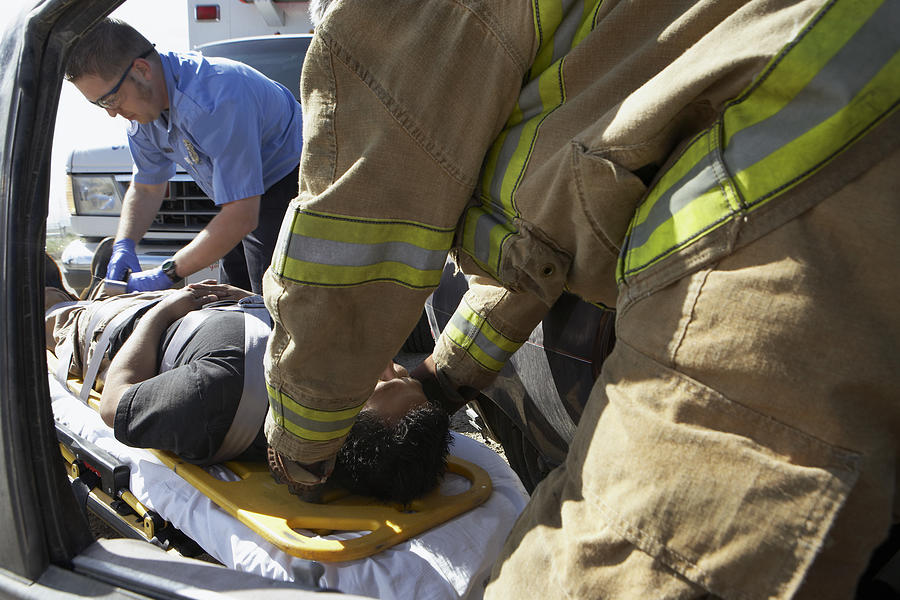Firefighter and paramedics taking victim out of crashed car Photograph by Moodboard