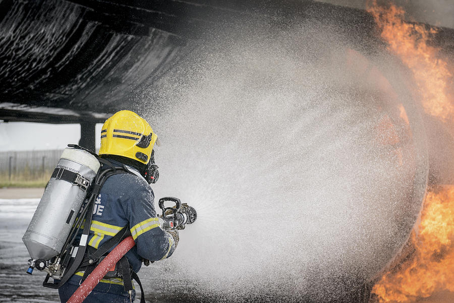 Fireman spraying water on simulated aircraft fire at training facility Photograph by Monty Rakusen