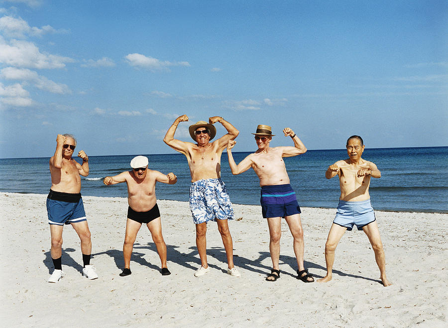 Five Senior Men in Swimming Trunks Stand on the Beach Flexing Their Muscles Photograph by Digital Vision.