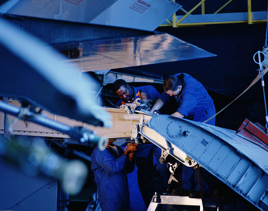Flight engineers working on wing flap of airplane Photograph by Getty Images