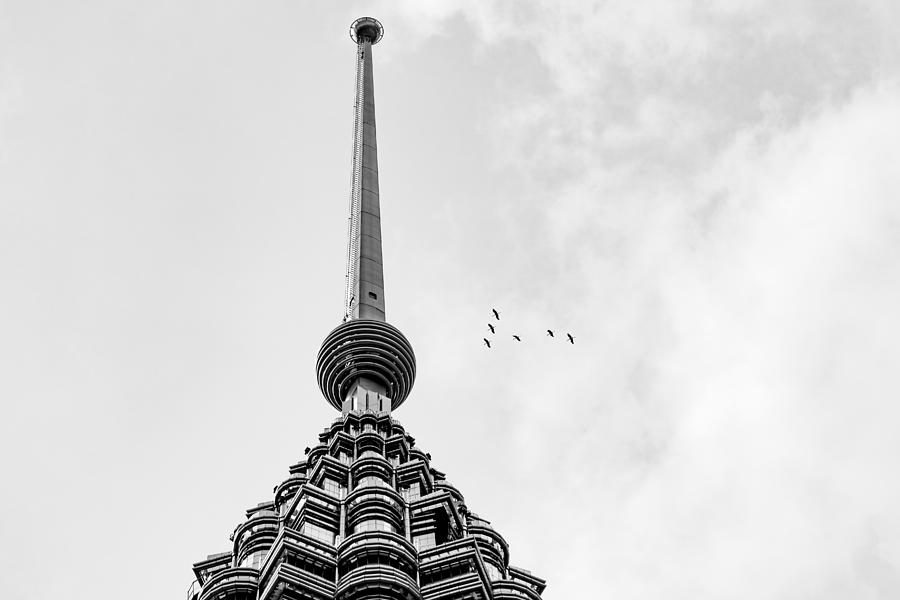 Flock of birds fly by over peak of Petronas Twin Towers. Photograph by Shaifulzamri