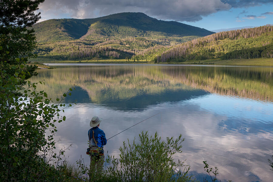 Fly fisherman at mountain lake with reflections, Colorado Photograph by Karen Desjardin