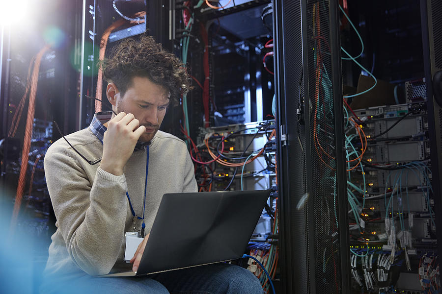 Focused male IT technician using laptop in server room Photograph by Caia Image