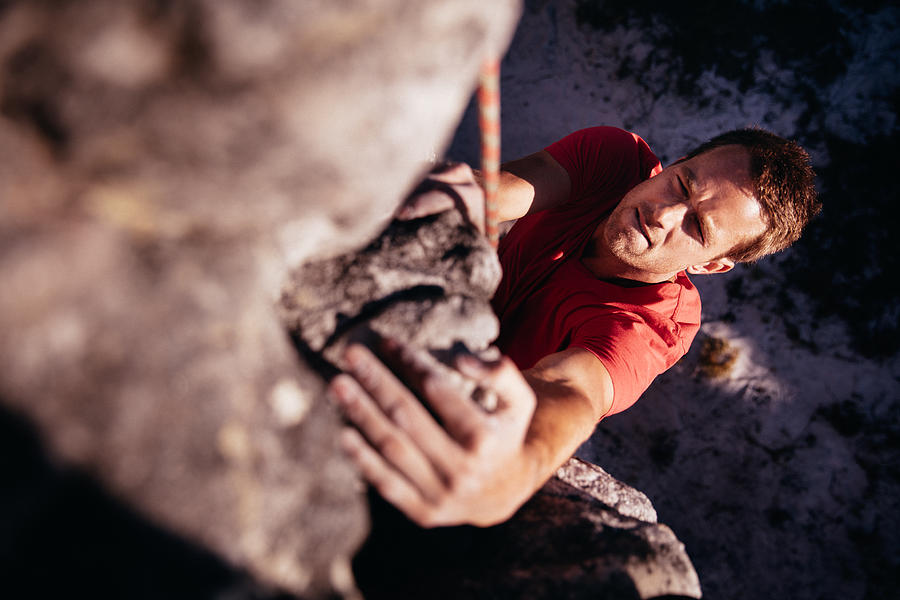 Focussed Rock climber holding on grip while hanging from boulder Photograph by Wundervisuals