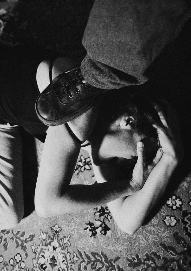 Foot standing on woman curled up on ground, close-up, b&w Photograph by Laurent Hamels