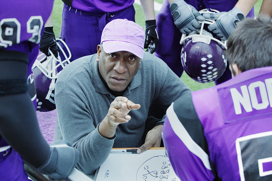 Football coach crouching, talking to team in huddle Photograph by Andersen Ross