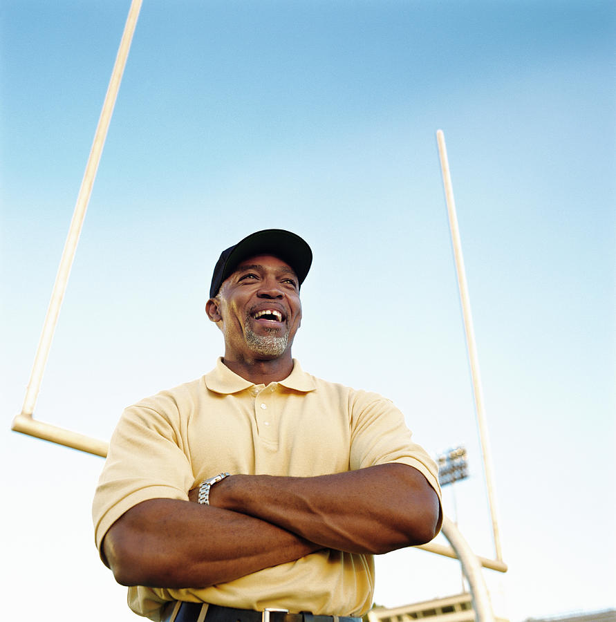 Football coach laughing, standing in front of goal post, low angle Photograph by Mike Powell