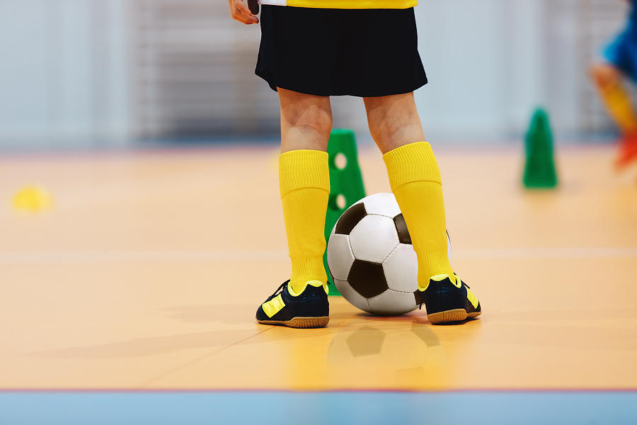 Football futsal training for children. Indoor soccer young player with a soccer ball in a sports hall. Soccer training dribbling cone drill. Player in blue uniform. Sport background. Photograph by Matimix