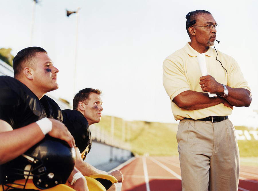 Football players with coach, watching game from side lines Photograph by Mike Powell