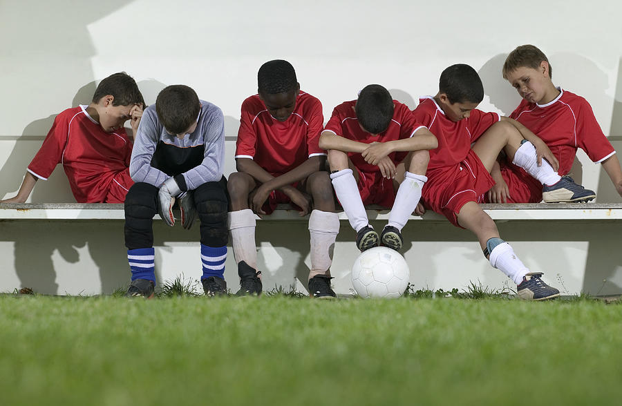 Football team of boys (8-12) sitting on bench, looking down Photograph by Photo and Co