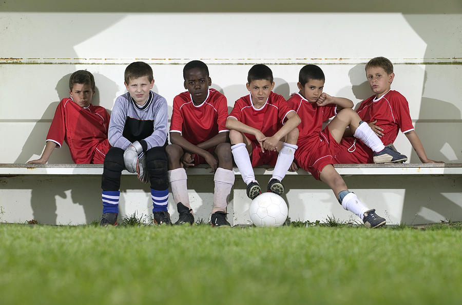 Football team of boys (8-12) sitting on bench, portrait Photograph by Photo and Co