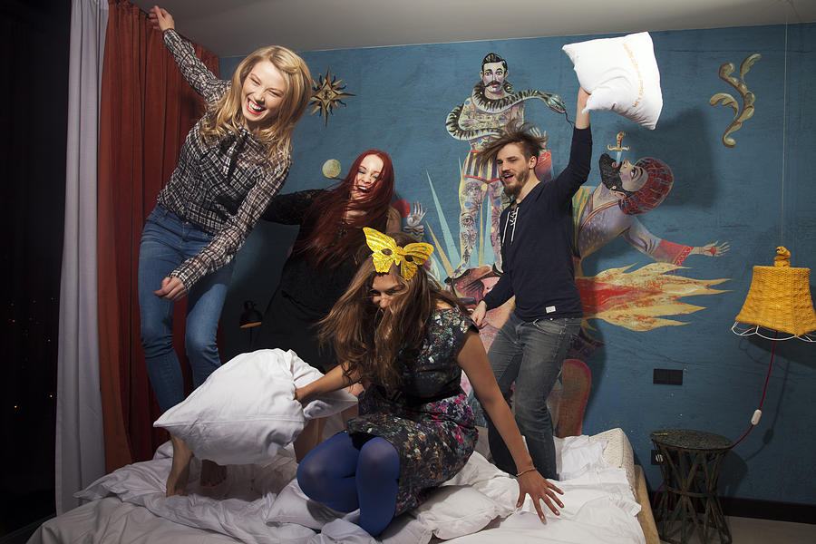 Four adult friends having pillow fight on hotel bed Photograph by Manuela