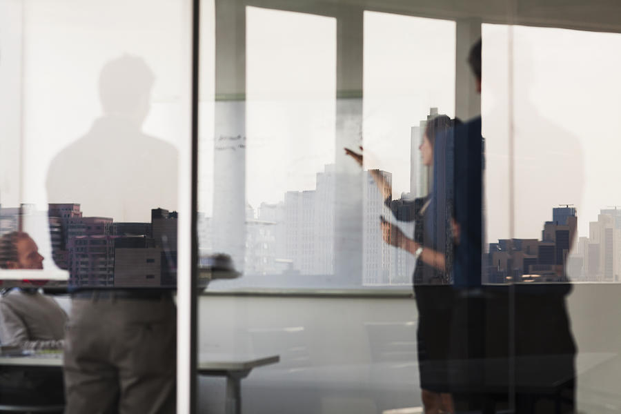 Four business people standing and looking at a white board on the other side of a glass wall Photograph by XiXinXing