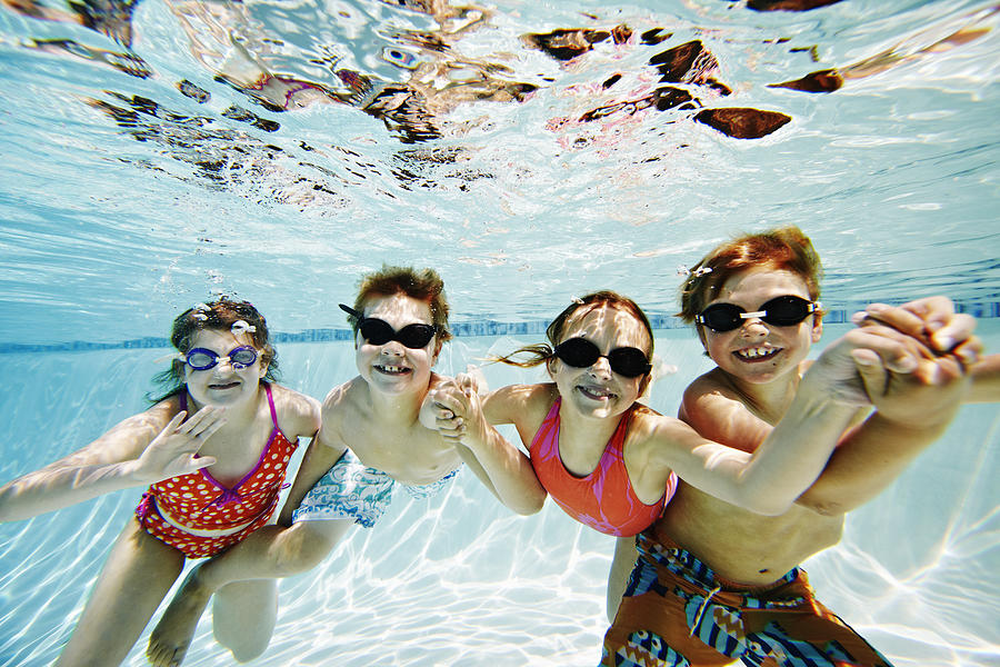 Four children underwater in pool smiling Photograph by Thomas Barwick