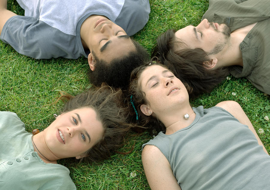 Four friends lying on grass with heads together Photograph by Odilon Dimier