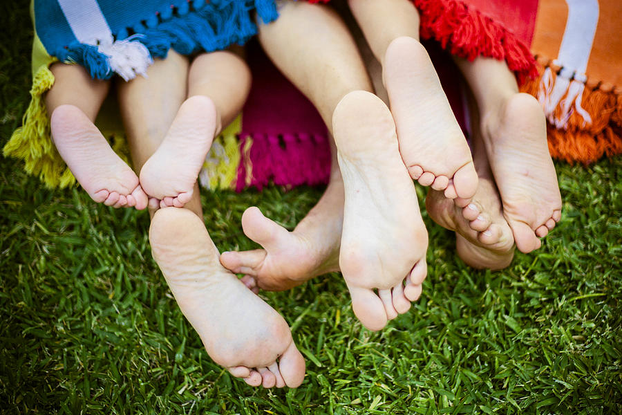 Four pairs of feet stick out the end of a colorful blanket on the grass Photograph by Anadorado