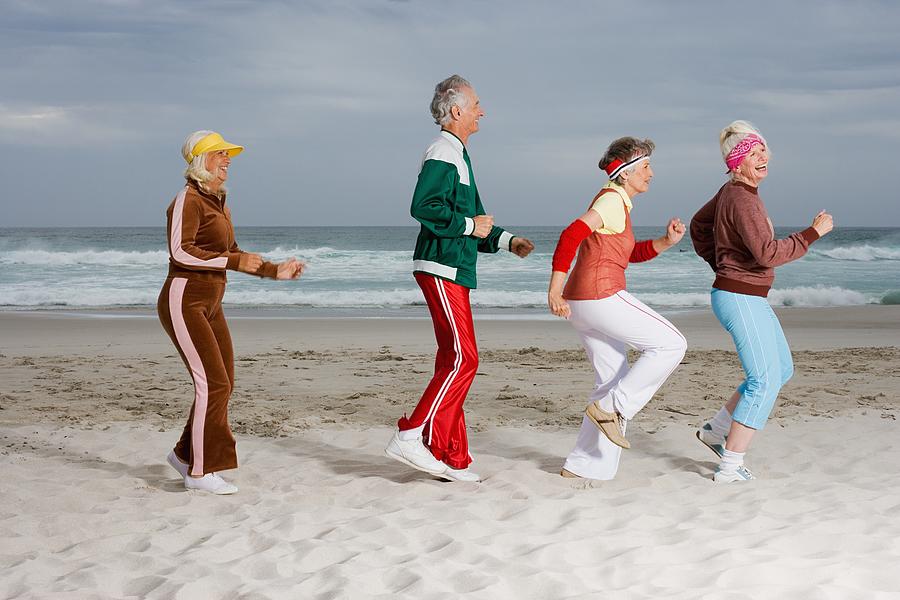 Four senior adult running on the beach Photograph by Image Source