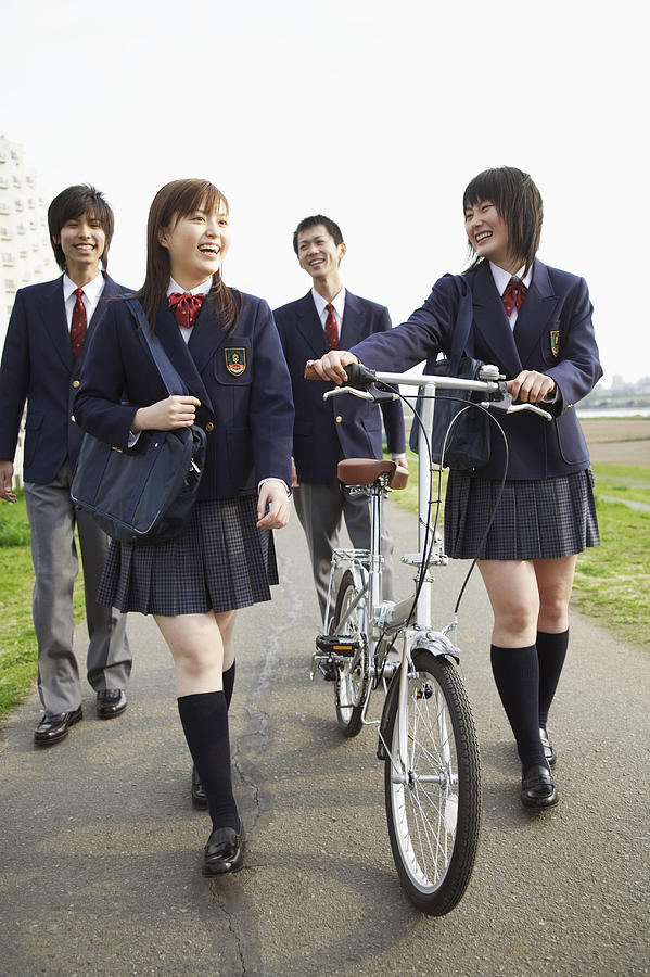 Four Students in Uniform Walking Outdoors, One Holding a Bicycle Photograph by Digital Vision.