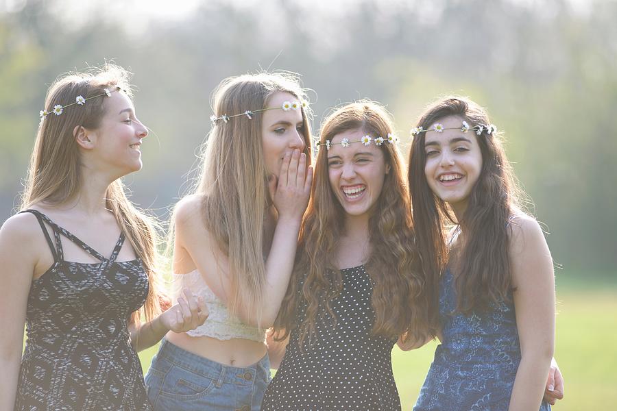 Four teenage girls wearing daisy chain headdresses giggling in park Photograph by Peter Muller