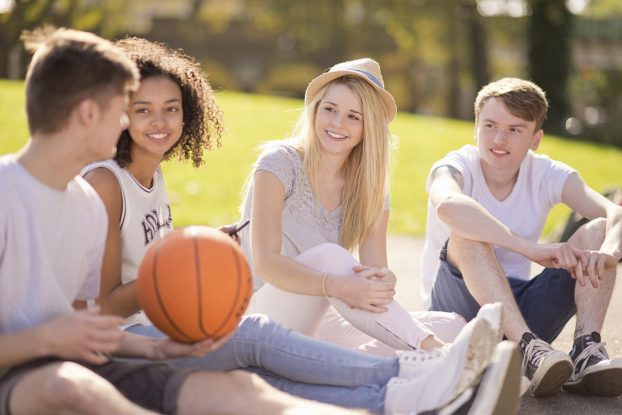 Four young adult basketball players sitting chatting Photograph by Ben Pipe Photography