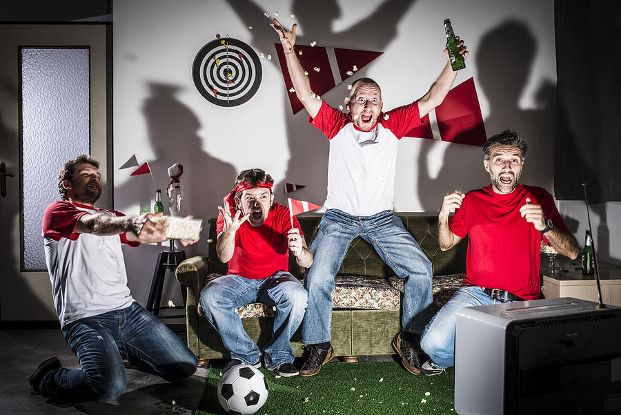 Four young adult men friends watching football on television: Goal! Photograph by Ilbusca