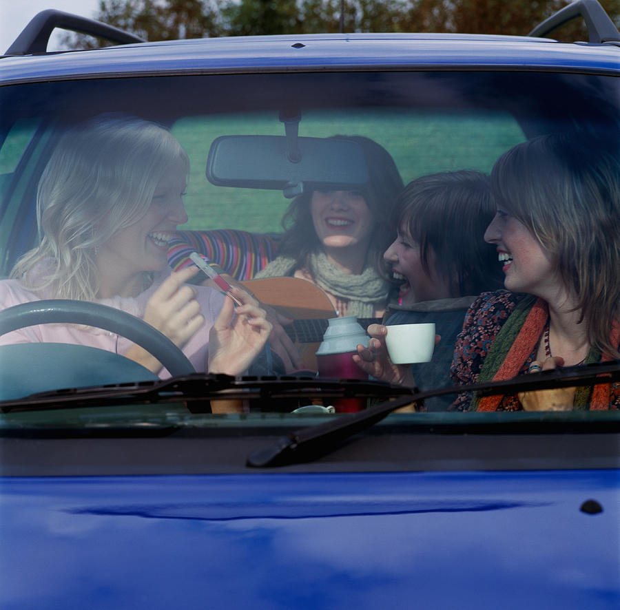 Four young women in car, laughing, view through front window Photograph by Frank Herholdt