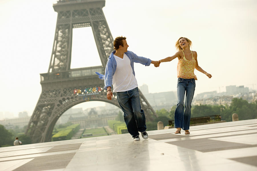 France, Paris, couple holding hands while running, smiling Photograph by Digital Vision.