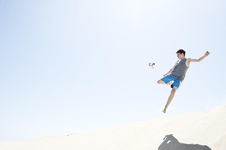 France, Teenage boy jumping on sand dune after football Photograph by Westend61