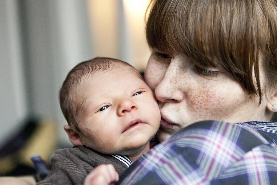 Freckled mother kissing her newborn baby son on the cheek Photograph by Westend61