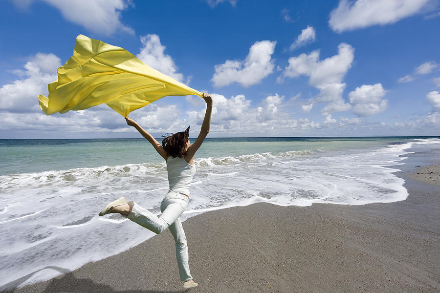Freedom - Woman jumping seaside holding yellow scarf in wind Photograph by RelaxFoto.de