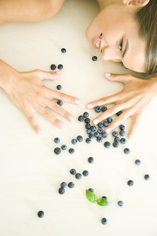 Fresh blueberries scattered across counter, young woman spreading hands over them Photograph by PhotoAlto/Rafal Strzechowski