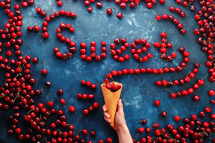 Fresh cherries in a waffle ice cream cone forming a word Sweet on a stone background with copy space. Food typography or food lettering concept with ripe berries Photograph by Dina Belenko Photography