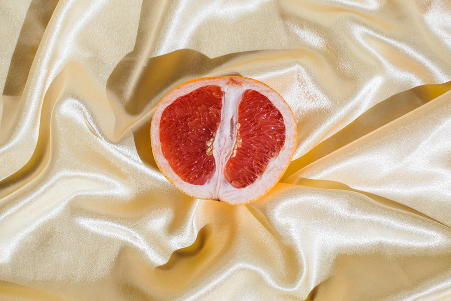 Fresh grapefruit on beige soft silk fabric background. Sex concept. Womens health, sexuality, erotic tension. Female vagina and clitoris symbol. Photograph by Tanja Ivanova