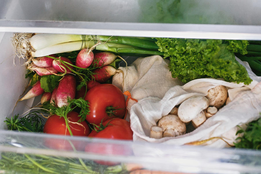 Fresh vegetables in opened drawer in refrigerator. Plastic free carrots,tomatoes, mushrooms,onions, radish,salad, arugula from market in fridge. Zero waste grocery shopping concept. Photograph by Bogdan Kurylo