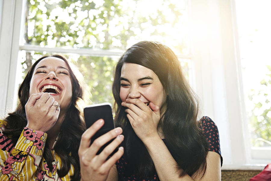Friends laughing at a mobile phone Photograph by Ezra Bailey