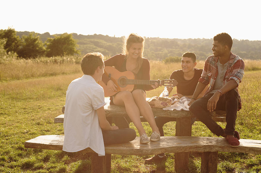 Friends playing music together at picnic table in rural field Photograph by Jacobs Stock Photography Ltd