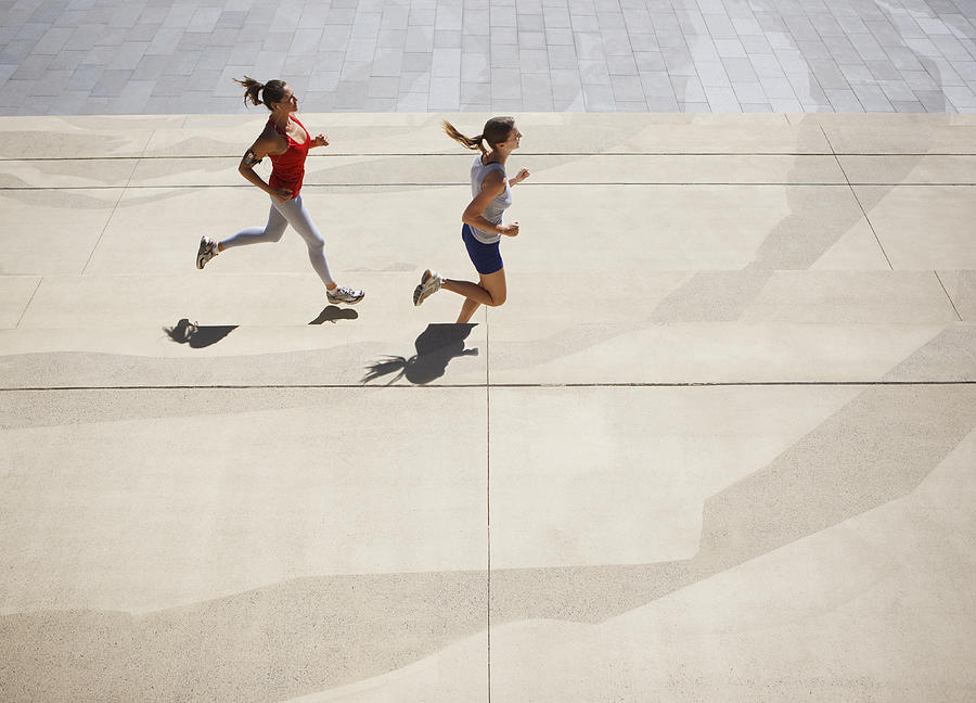 Friends running along urban sidewalk Photograph by Paul Bradbury