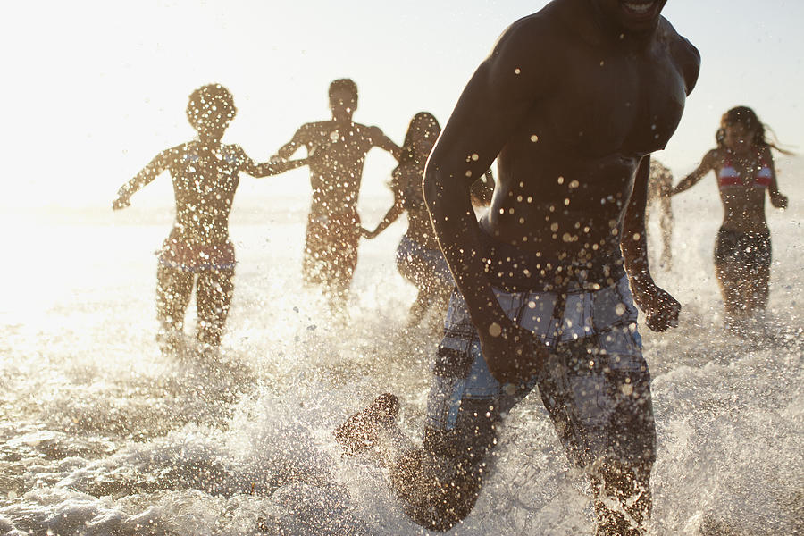 Friends splashing in waves on beach Photograph by Sam Edwards