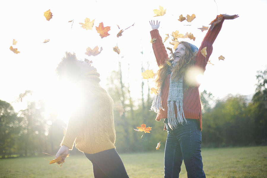 Friends throwing autumn leaves in air Photograph by Peter Muller
