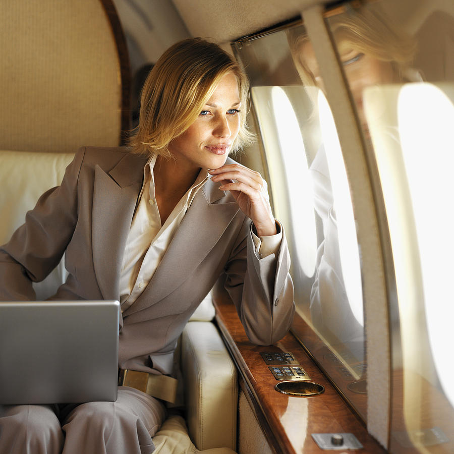 Front View Of Businesswoman Sitting Holding Laptop On Her Lap Looking Out Window In First Class Airplane Photograph by Stockbyte