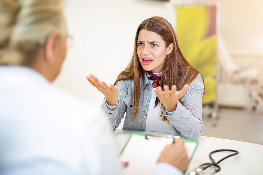 Frustrated young woman talking with her doctor. Photograph by DjelicS
