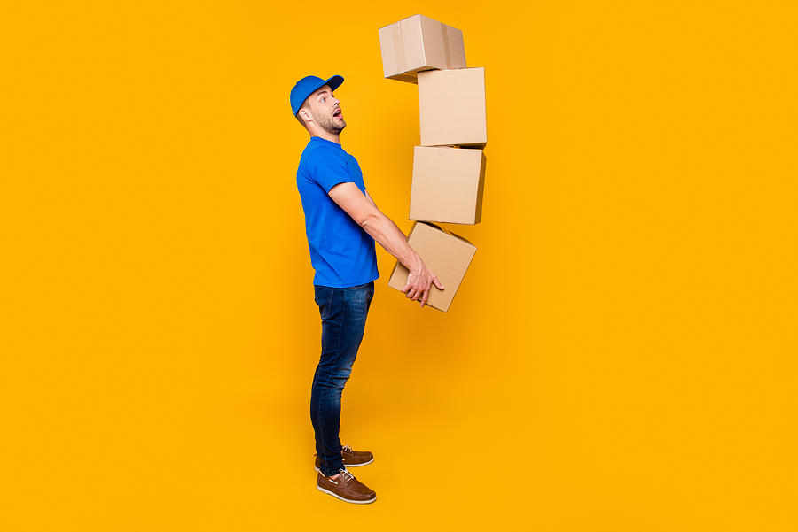 Full body length size, side profile view of handsome scared, shocked bearded deliver in uniform holding four large big flying up in air boxes in arms, isolated over bright vivid yellow background Photograph by Deagreez