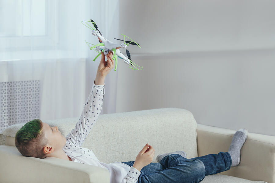 Full length of boy lying on sofa holding drone at home Photograph by Vasily Pindyurin