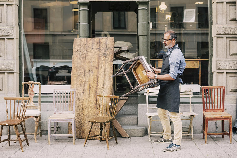 Full length of man holding chair while arranging outside store Photograph by Maskot