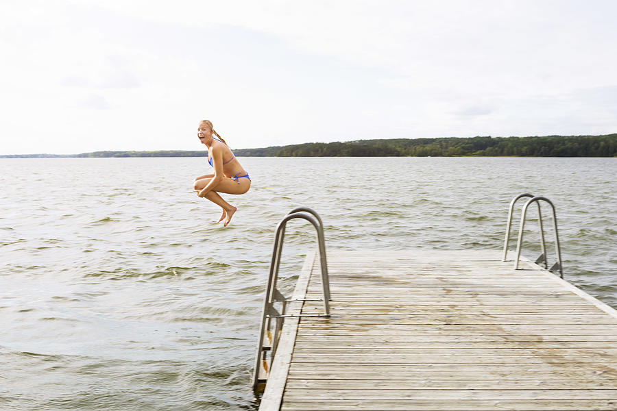Full length side view of excited woman jumping into lake Photograph by Maskot