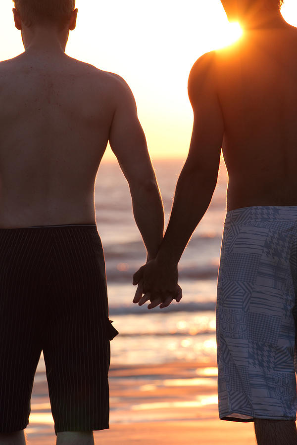 Gay couple holding hands on beach Photograph by Peter Cade
