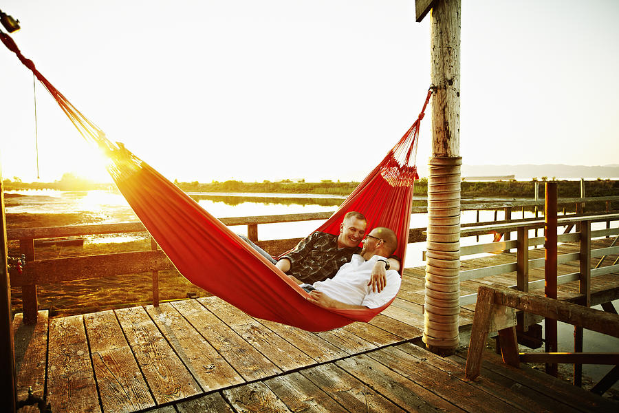 Gay couple in hammock on dock at sunset Photograph by Thomas Barwick