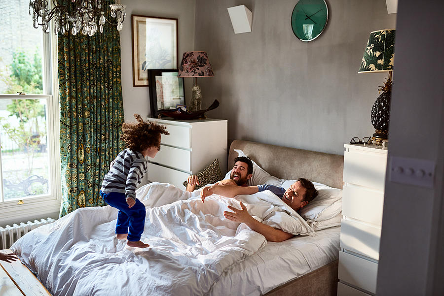 Gay couple waking up with young son jumping on bed Photograph by 10000 Hours