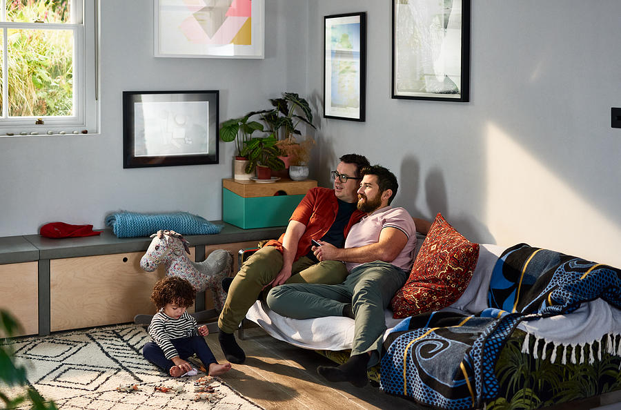 Gay couple watching television with son playing on floor Photograph by 10000 Hours